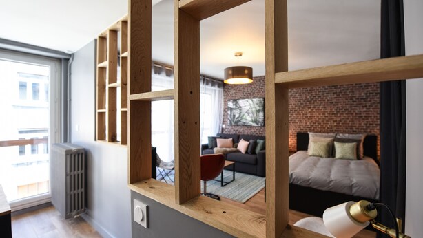 Ein modernes Zimmer mit einem großen Spiegel, Holzregalen, einem Bett, einer Couch und einem Essbereich.