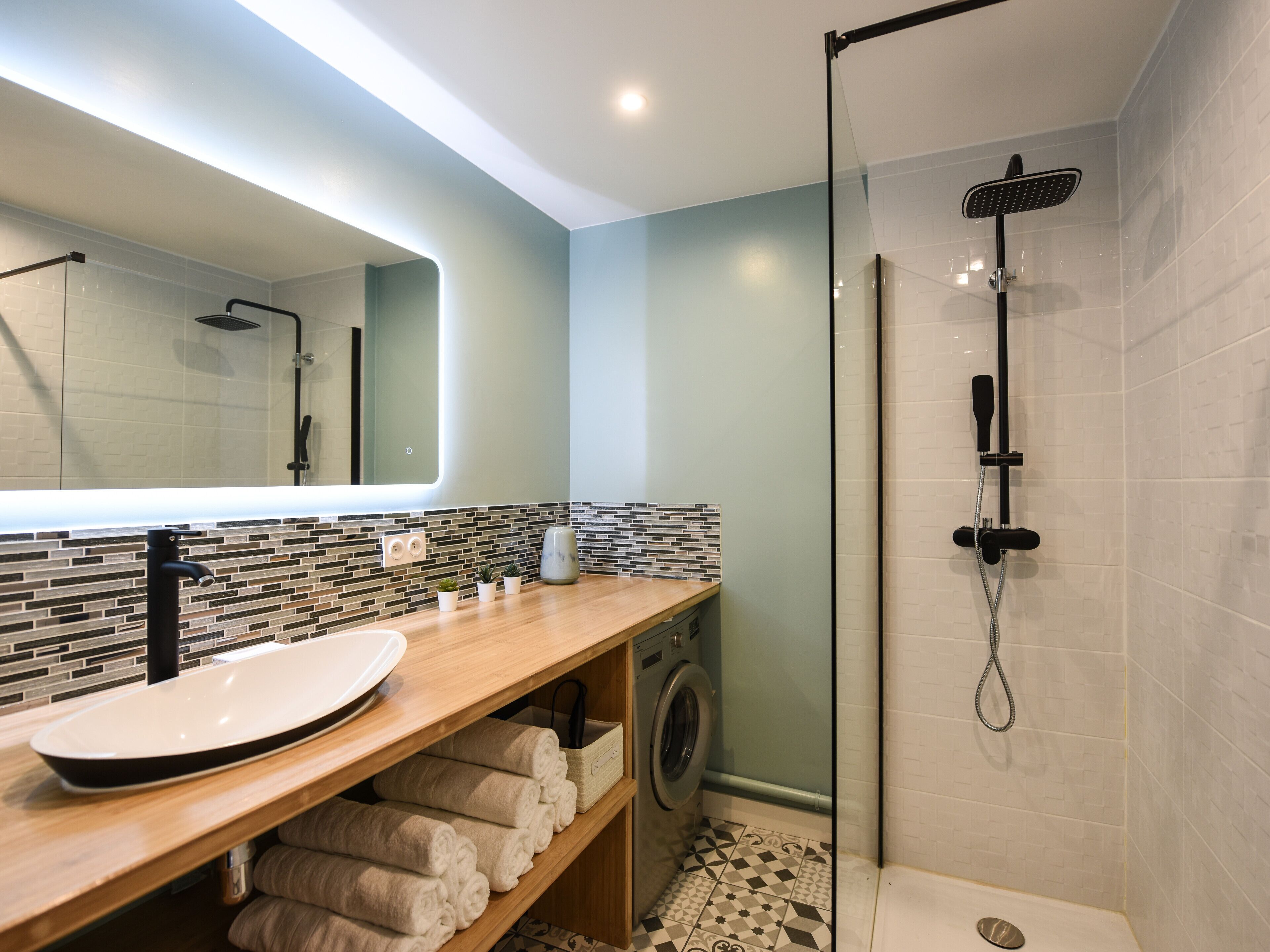 A modern bathroom with a glass-enclosed shower, a wooden vanity with a sink, and a built-in washing machine.
