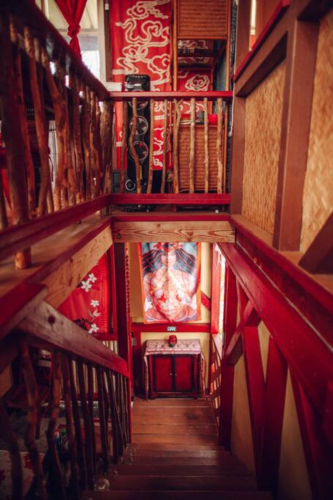 A narrow wooden staircase with red railings and a traditional Chinese painting at the bottom.