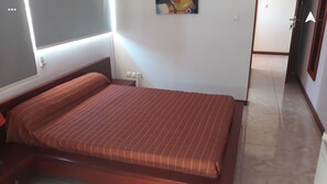 A small, single-bed room with a wooden headboard, a plain wall, and a tiled floor.