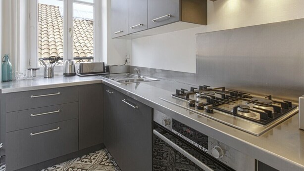A modern kitchen with grey cabinets, stainless steel appliances, and a window with a patterned view. - Appartement Bourbon - Welkeys (Bayonne)