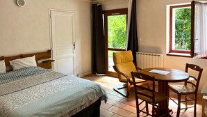 A bedroom with a bed, a chair, a table, and a window with a view of greenery. - Studio Serena - Welkeys (Seynod)