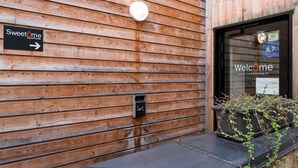 A wooden exterior wall with a sign for Sweetome apartment hotel, a door with a window displaying a price of 8.7, and a small planter with plants. - Palais Rinour - Cosy studio close to stations - Welkeys (Lille)