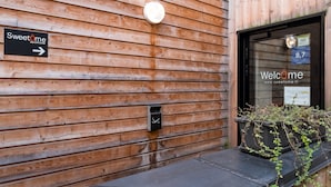 A wooden exterior wall with a sign for Sweetome apartment hotel, a door with a window displaying a price of 8.7, and a small planter with plants. - Vieille Bourse - Studio close to stations and old city - Welkeys (Lille)
