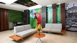 A modern lobby with two grey sofas, a wooden coffee table, and a vibrant parrot mural. - Hotel Cultura Plaza (San José)
