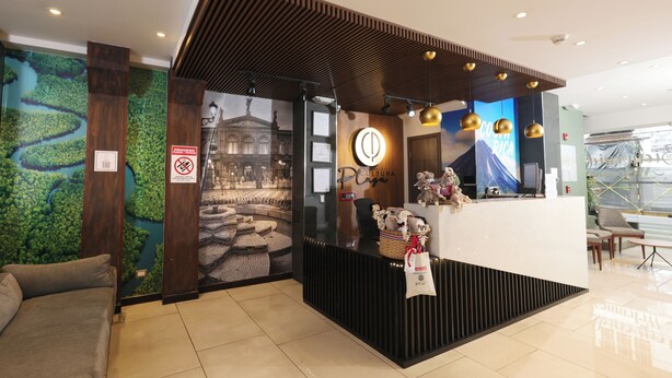 A reception area with a modern design, featuring a reception desk, a seating area with a sofa, and a wall with a mural. - Hotel Cultura Plaza (San José)