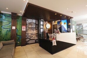 A reception area with a modern design, featuring a reception desk, a seating area with a sofa, and a wall with a mural. - Hotel Cultura Plaza (San José)