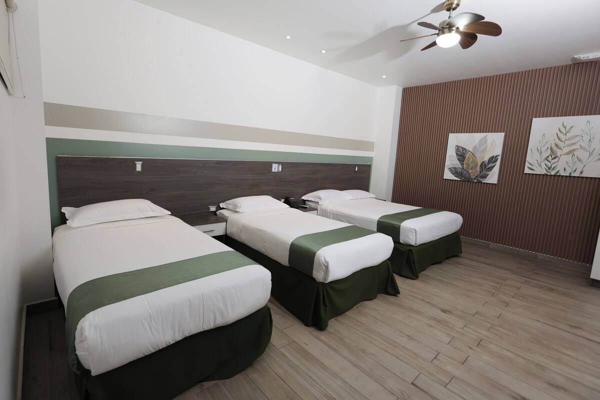 A hotel room with two single beds, a ceiling fan, and a wooden floor.
