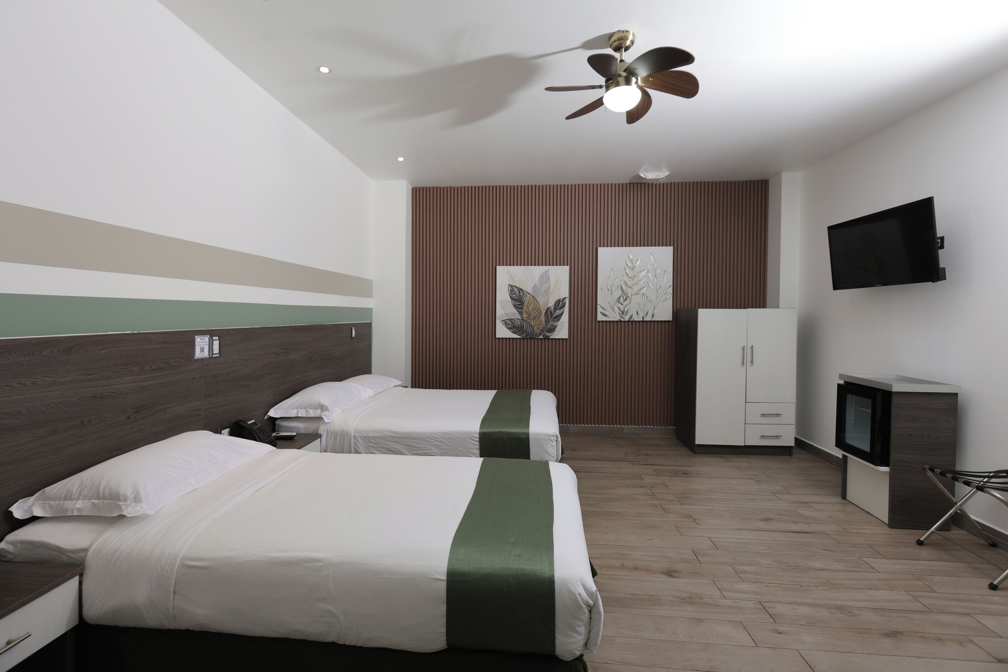 A hotel room with two beds, a ceiling fan, a TV, and a wardrobe.