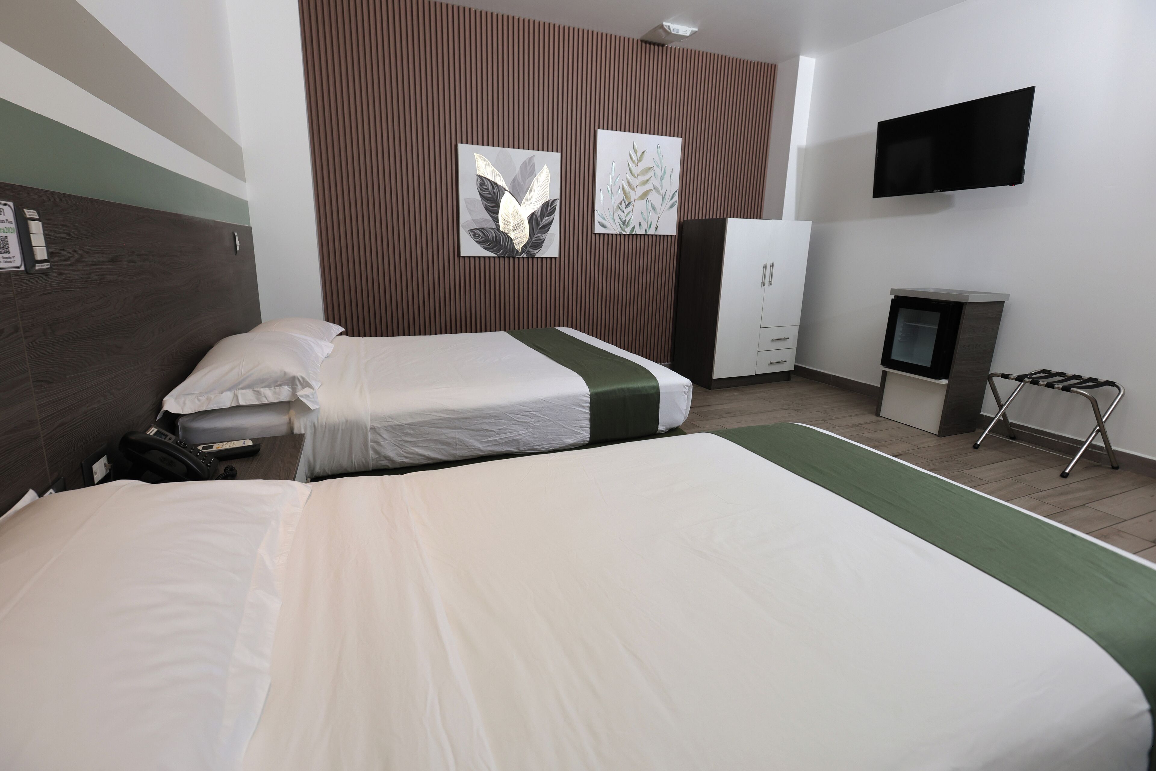 A hotel room with two beds, a TV, a wardrobe, and a small desk with a chair.