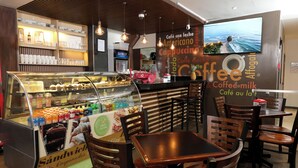 A café with a display case of pastries and a seating area with wooden tables and chairs. - Hotel Cultura Plaza (San José)