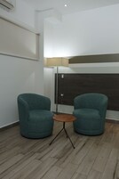 Una habitación con dos sillones turquesa, una mesita redonda pequeña, una lámpara y suelo de madera.