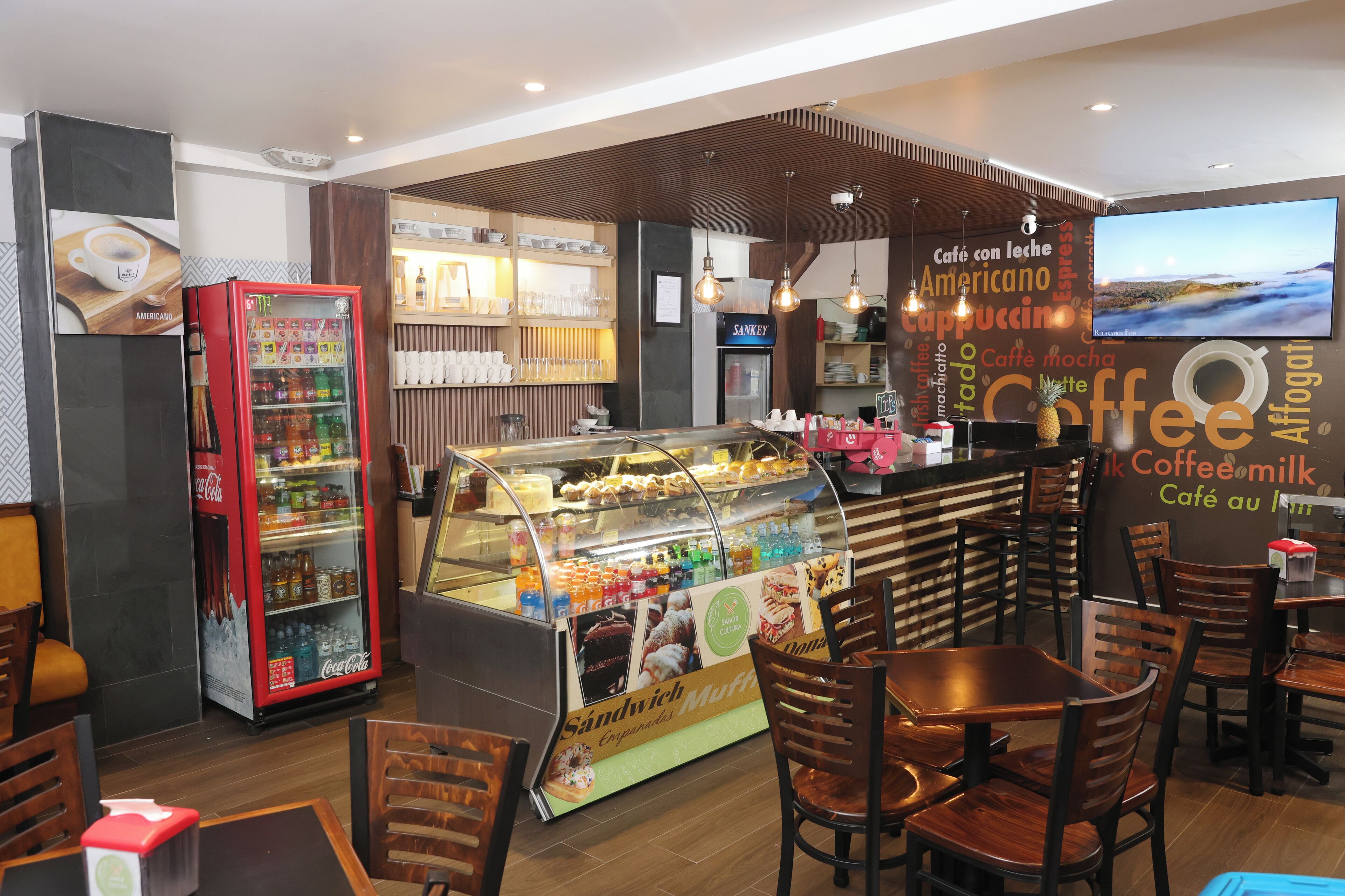A café with a display case of pastries, a Coca-Cola refrigerator, and wooden furniture.