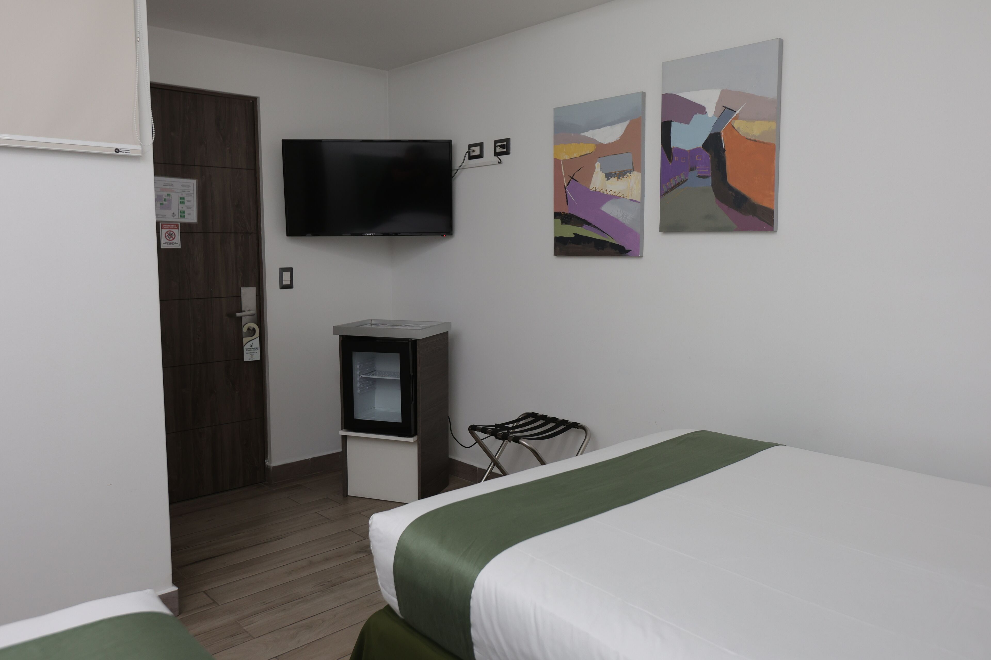 Ein Hotelzimmer mit einem Bett, einem Fernseher, einer kleinen Kommode und zwei abstrakten Bildern an der Wand.