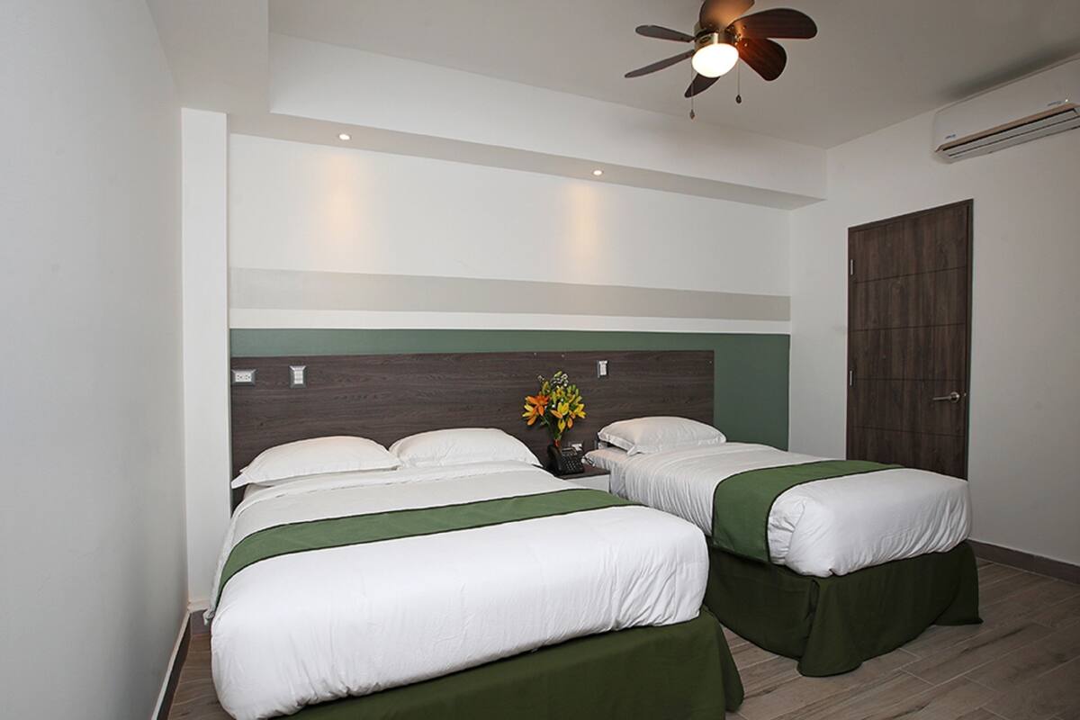 A hotel room with two beds, a wooden floor, a ceiling fan, and a door.