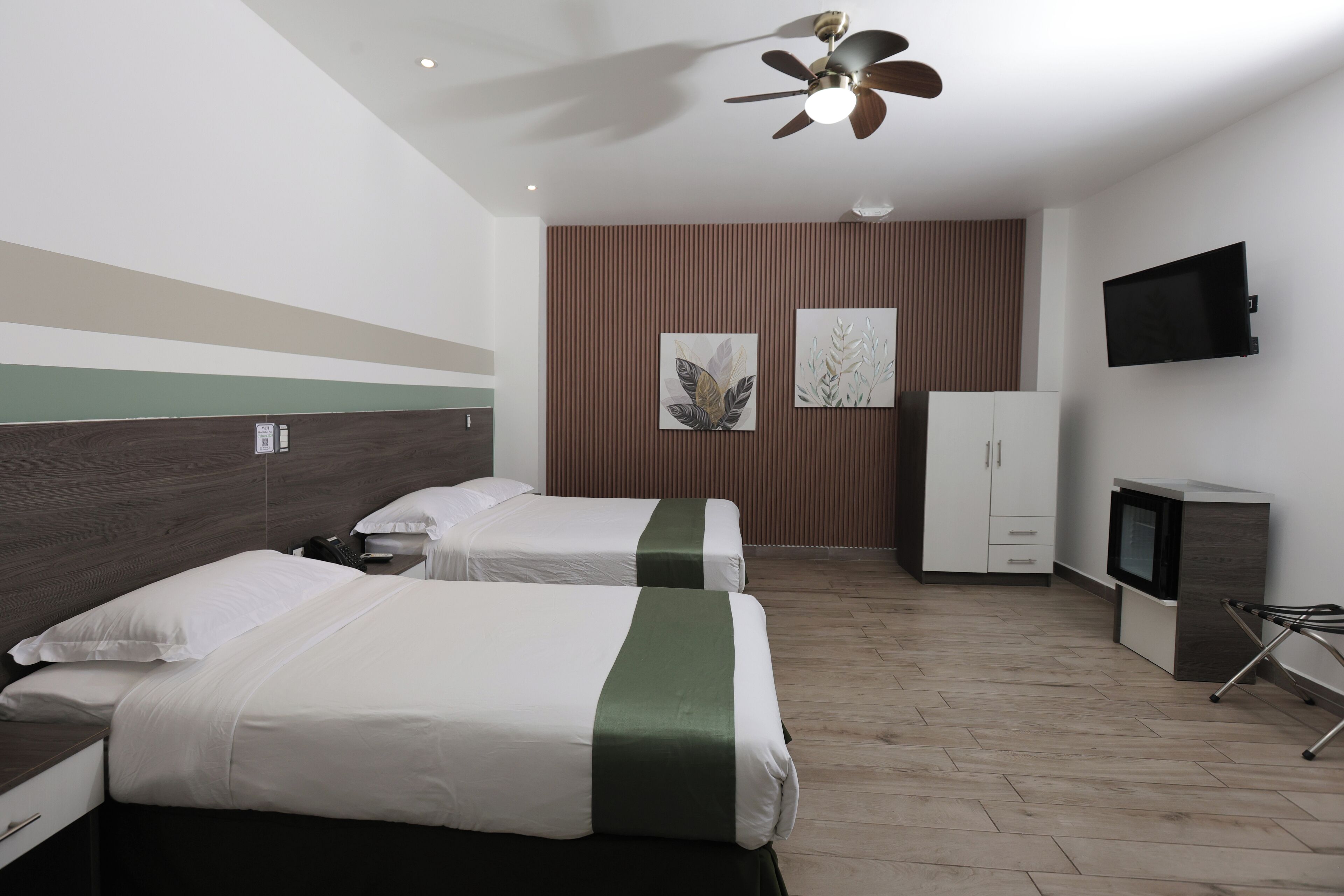 A hotel room with two beds, a ceiling fan, a flat-screen TV, and a cabinet.