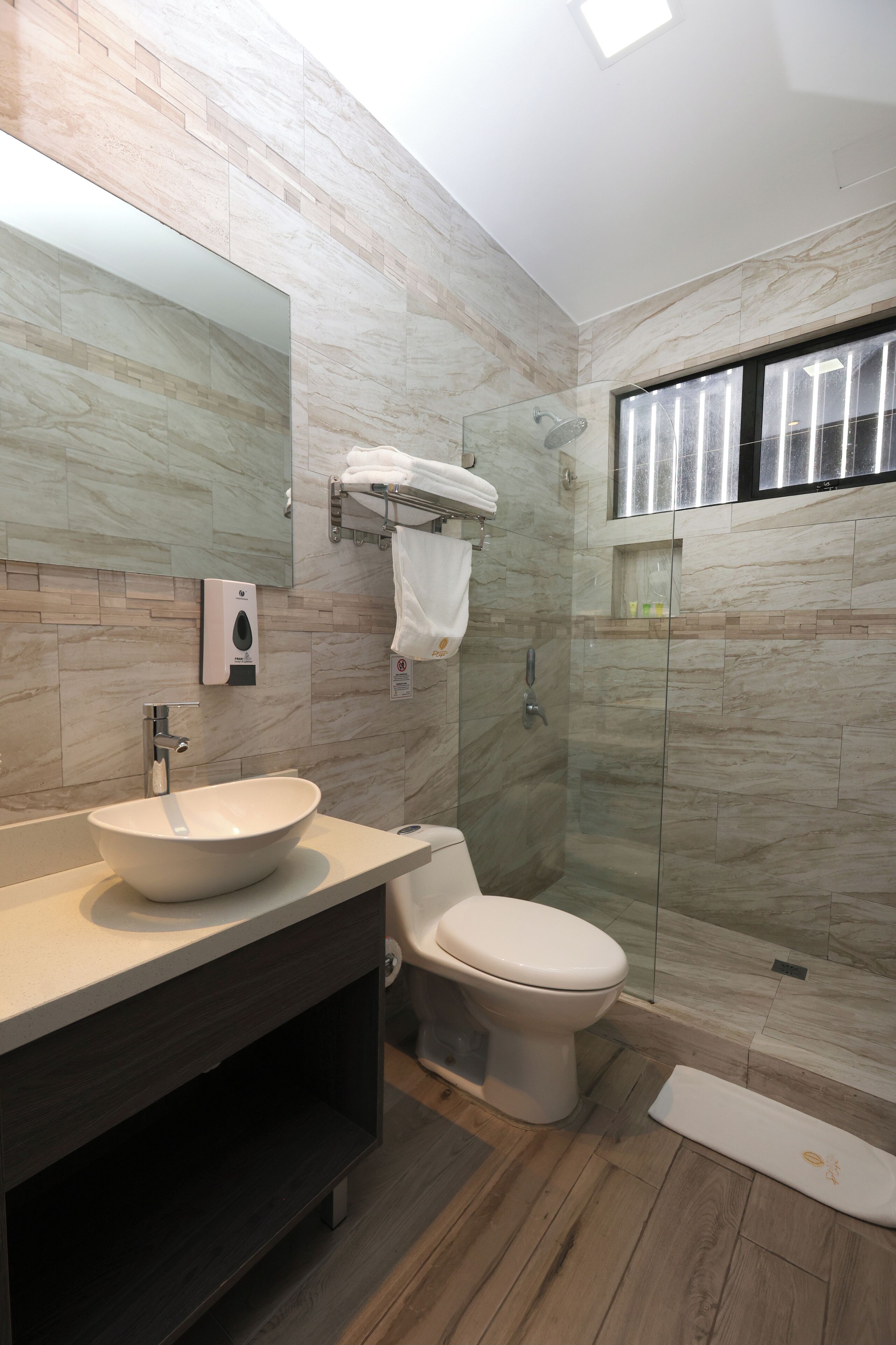 Une salle de bain moderne avec un pare-baignoire en marbre, un grand miroir, un lavabo blanc, des toilettes et une douche à parois de verre.