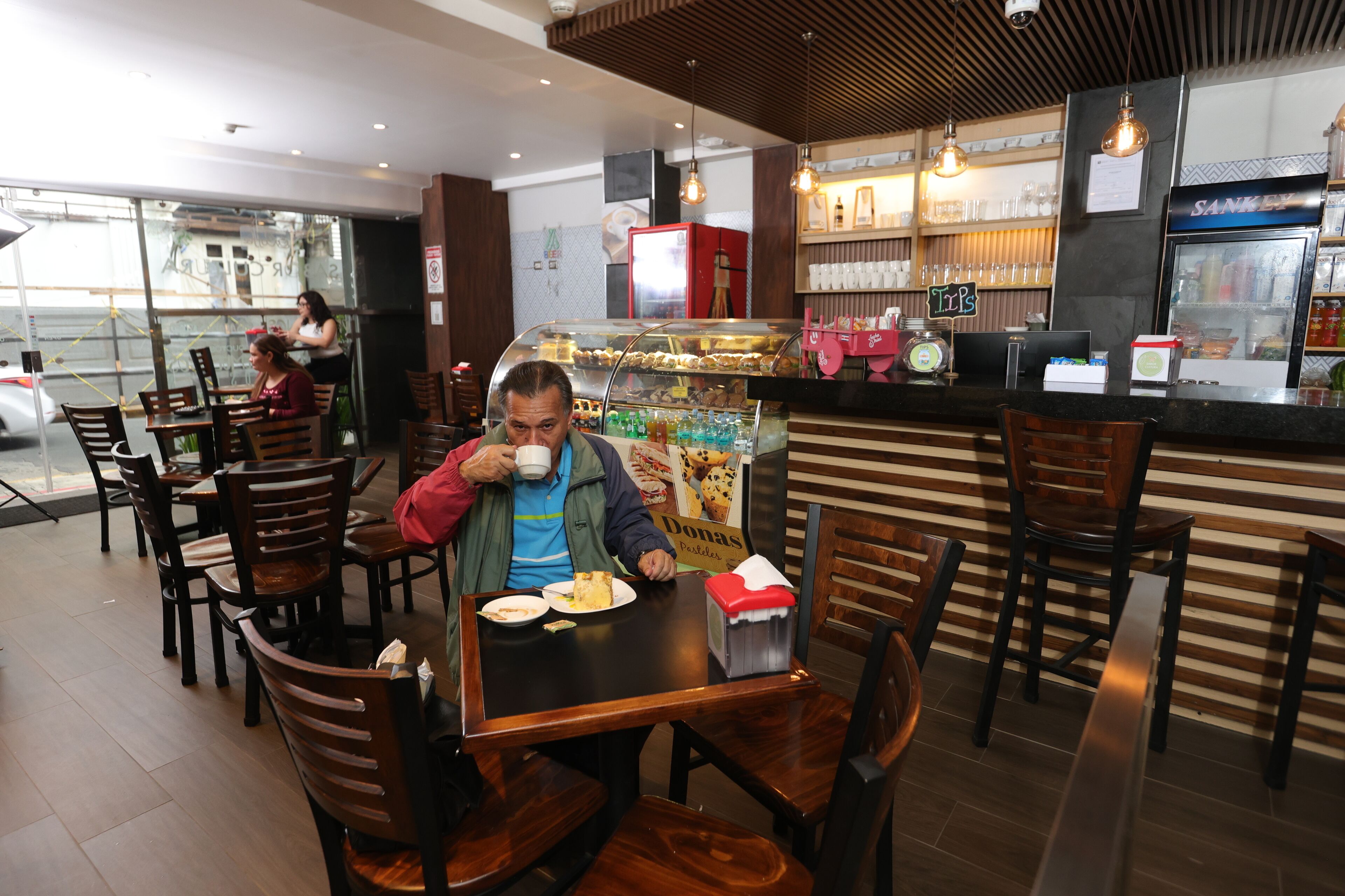 A restaurant with wooden chairs and tables, a counter with a display case, and a refrigerated display.