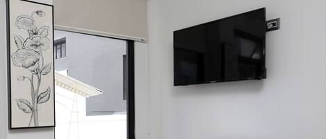 Una habitación moderna con un ventanal grande, un televisor de pantalla plana, un mini refrigerador integrado y un tendedero pequeño.