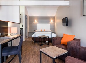 Ein kleines Hotelzimmer mit Bett, Schreibtisch, Stuhl, einem kleinen Tisch und einer Couch.