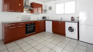 A compact kitchen with brown cabinets, a stainless steel range hood, a microwave, a dishwasher, and a washing machine. - Triplex Laharie - Welkeys (Bayonne)