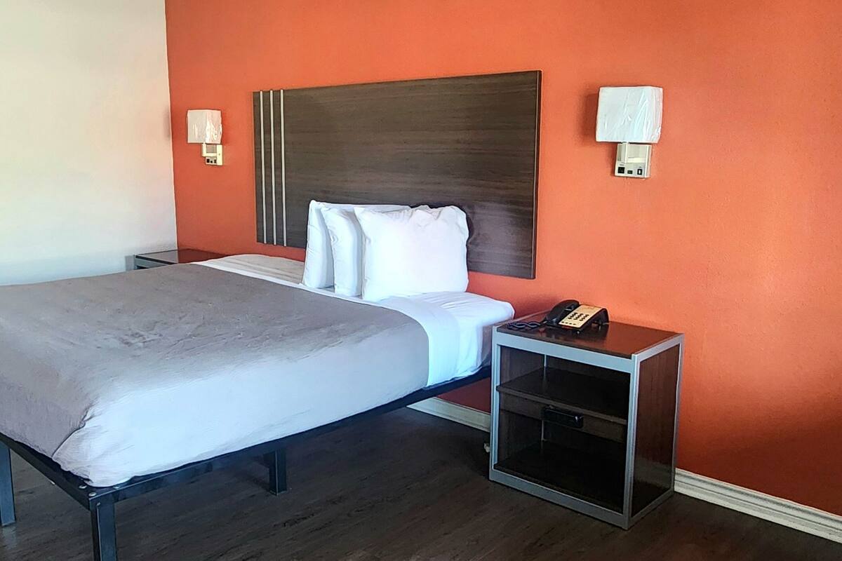 A hotel room with a bed, a nightstand, a telephone, and two wall-mounted lamps.