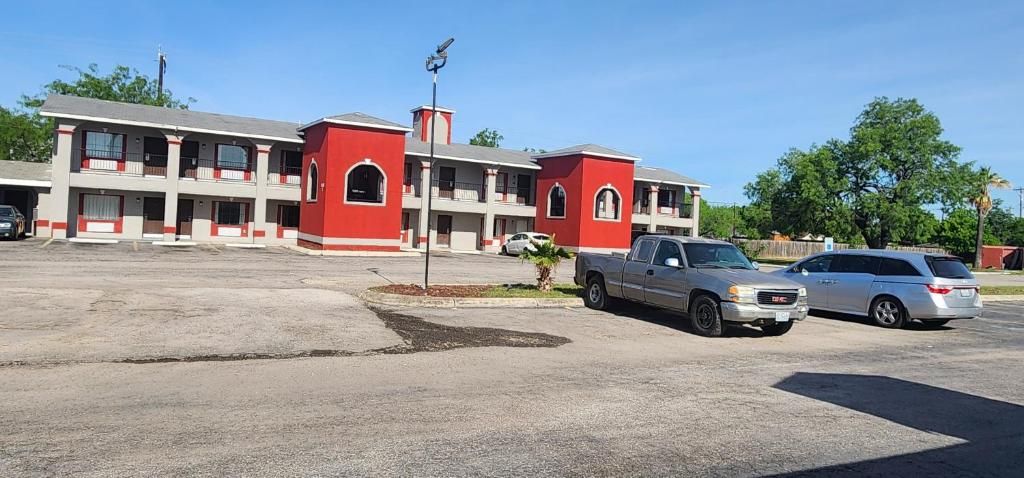 A motel with a red and white facade, multiple balconies, and a parking lot with two vehicles.