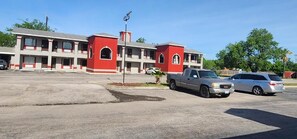 A motel with a red and white facade, multiple balconies, and a parking lot with two vehicles. - Econo Inn Lackland AFB Seaworld (San Antonio)