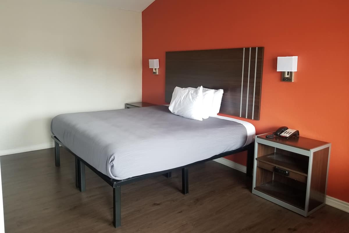 A hotel room with a bed, bedside table, lamp, and a phone.