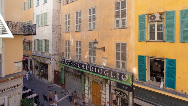 A street view with a building labeled "CAVES CAPRIOGLIO" and "MUSSEUX" with a sign for "Rôtisserie du Palet". - Appartement Verrière - Welkeys (Nice)