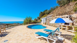 Une piscine en pierre, dotée de chaises longues et d’un espace barbecue, avec une vue imprenable sur une colline pittoresque.