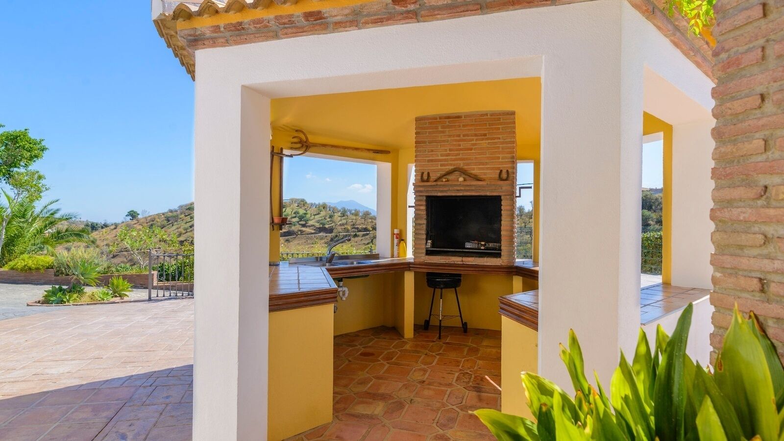Una cocina exterior compacta con una parrilla de ladrillo, un lavamanos y un taburete pequeño.