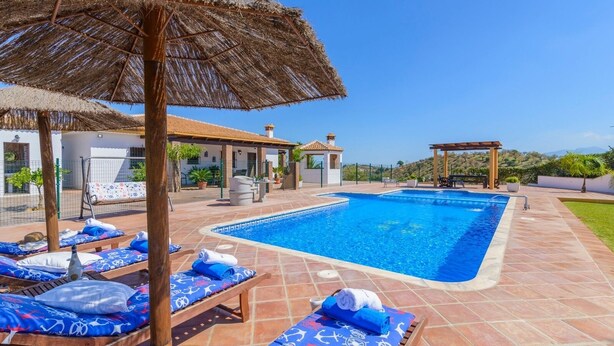 Une piscine entourée de chaises longues et de parasols, avec une terrasse offrant une vue sur une colline.