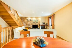 A living room with a wooden staircase, a fireplace, a TV, and a dining table with a floral centerpiece.