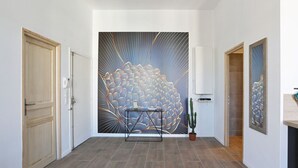 A hallway with a large abstract mural, a potted plant, and a metal table. - Appartement Carnot - Welkeys (Cannes)