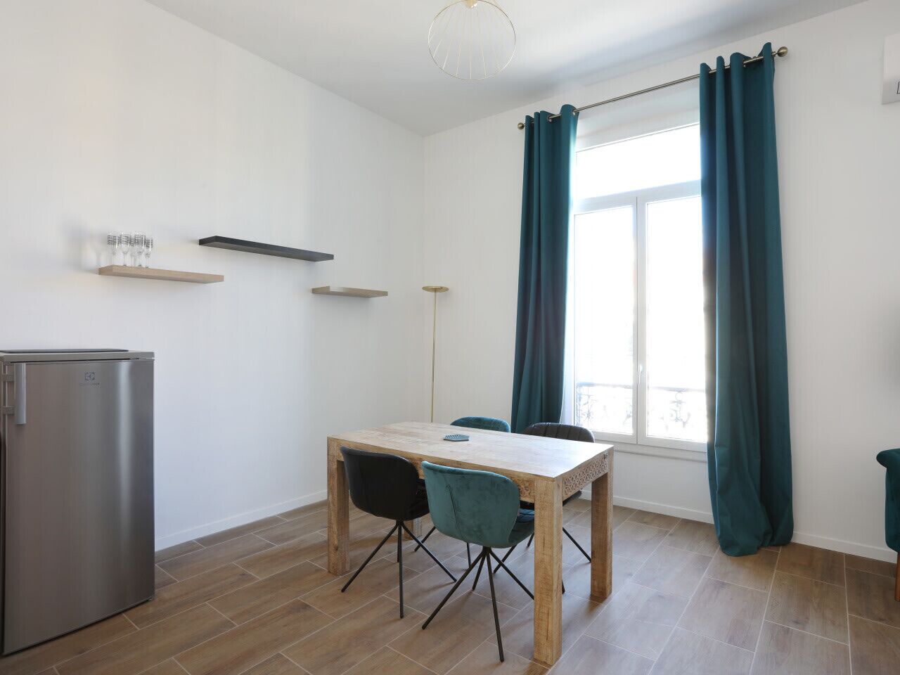 Eine kleine Küche mit einem Holztisch, zwei Stühlen, einem Kühlschrank und lindgrünen Vorhängen.