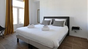 A modern hotel room with a large bed, two pillows, a bedside table, and a chair. - Appartement Carnot - Welkeys (Cannes)