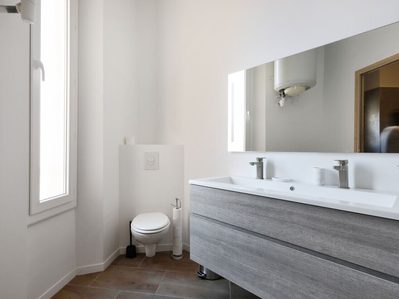Un baño moderno con inodoro, un espejo grande y tocador con lavabo.