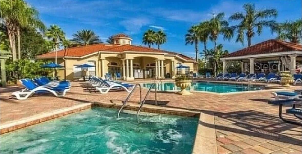 Een resort met een zwembad, ligbedden en palmbomen.