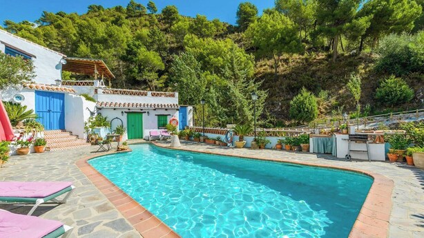 Un área de piscina con un edificio blanco, puertas azules y un camino de piedra.