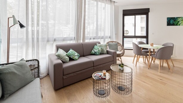 A modern living room with a sofa, a dining table with chairs, and a large window with sheer curtains. - Appartement Céladon - Welkeys (Lyon)