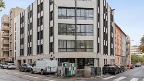 A modern multi-story building with a flat facade, large windows, and a ground-level entrance. - Appartement Céladon - Welkeys (Lyon)