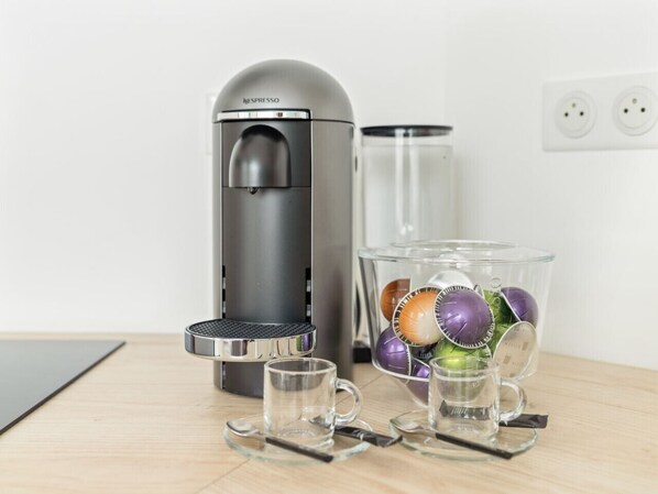 A Nespresso coffee machine, a glass container with coffee capsules, and a mug on a wooden table.
