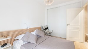 A modern bedroom with a large bed, a bedside table, a chair, and a wardrobe. - Appartement Céladon - Welkeys (Lyon)