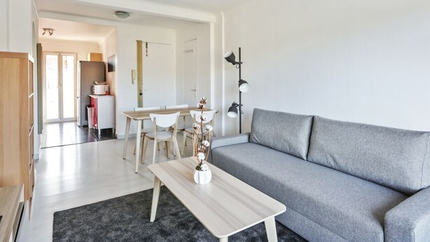 Ein modernes Wohnzimmer mit grauem Sofa, einem Holztisch und einem Essbereich mit weißem Tisch und Stühlen.