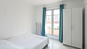 Ein Schlafzimmer mit einem Bett, einem Kleiderschrank, einem Heizkörper und einem Fenster mit Vorhängen.