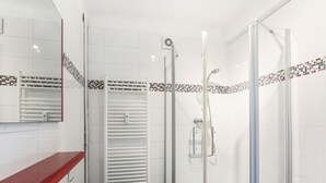 Ein modernes Badezimmer mit einer gläsernen Duschkabine, einem weißen Waschbecken mit roter Arbeitsplatte und einem gefliesten Duschbereich mit dekorativem Bordstein.
