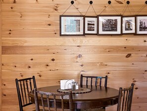 A wooden-paneled wall with framed pictures, a round table with chairs, and a salt and pepper set.