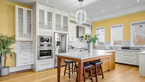 Una cocina moderna con armarios blancos, electrodomésticos de acero inoxidable y una isla central con taburetes.