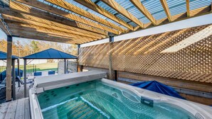 Un área de hidromasaje con un pérgola de madera, una zona de estar cubierta y una piscina.